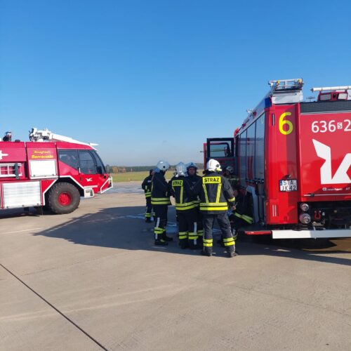 Strażacy obsługują wóz strażacki na tafli lotniska. Jest piękna, słoneczna pogoda.